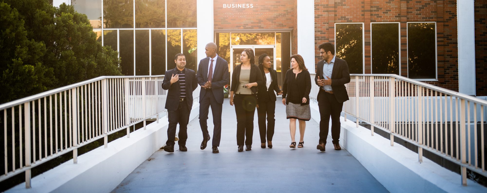 A group of business students talking to eachother while walking outside the business building.