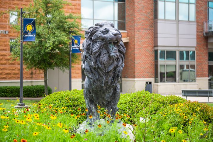 A lion statue with spring flowers blooming at its base on campus at A&M-Commerce.