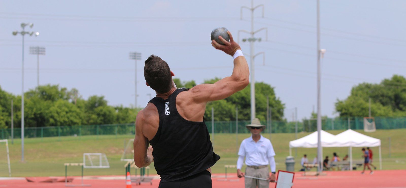 A male athlete competing in the shot put event launches a shot into the air.