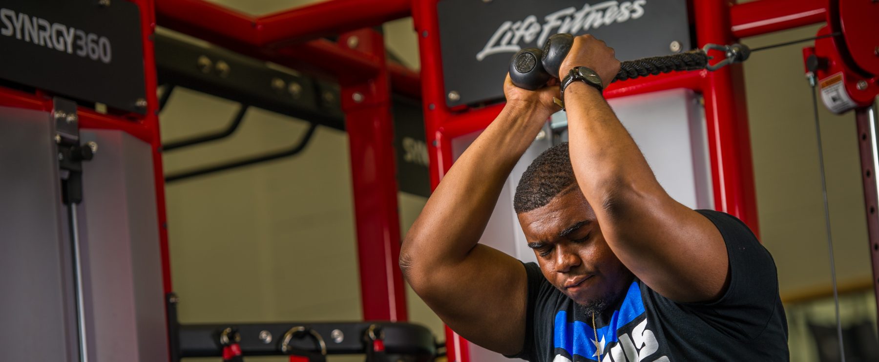 A student exercises on a machine inside a gym.