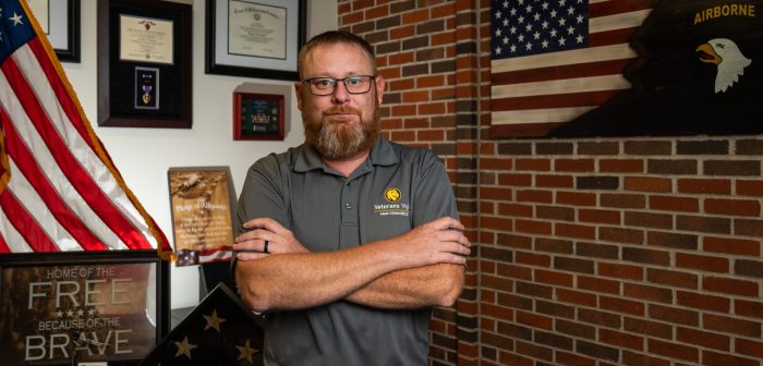 A person stands in front of a wall featuring various military medals and commendations.