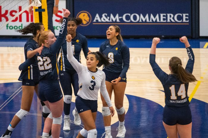 Six volleyball players cheer as they break from a huddle, with arms raised.