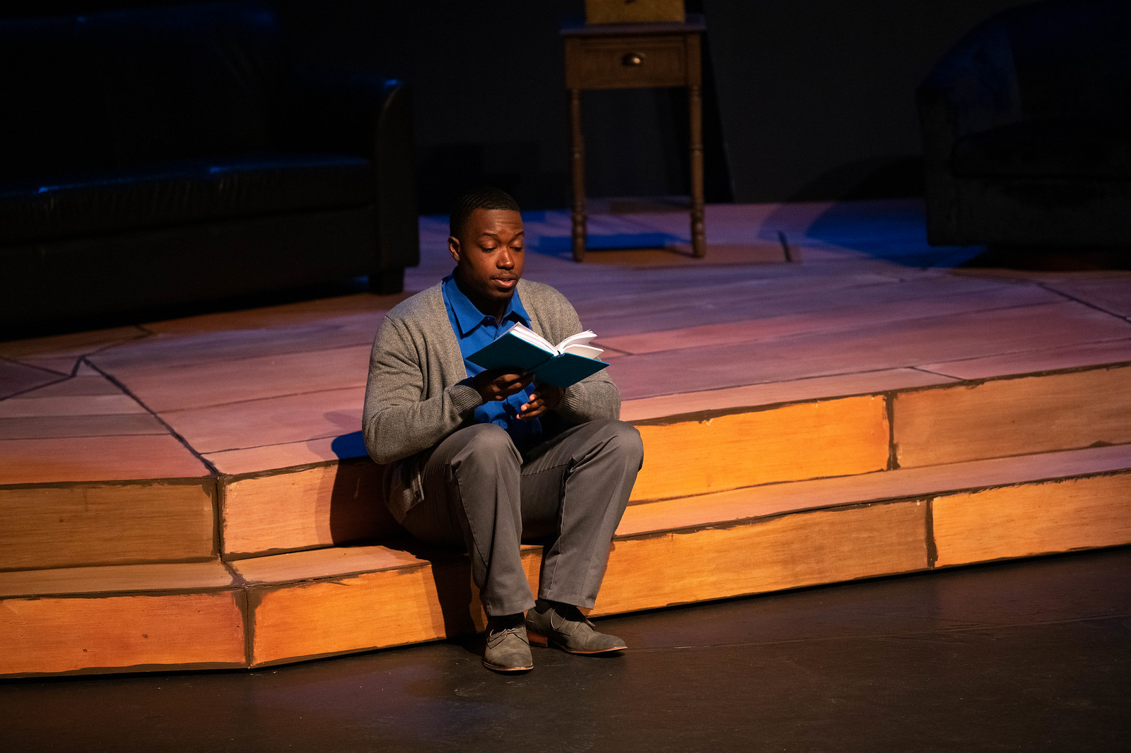 a male student sitting and reading a book in a play