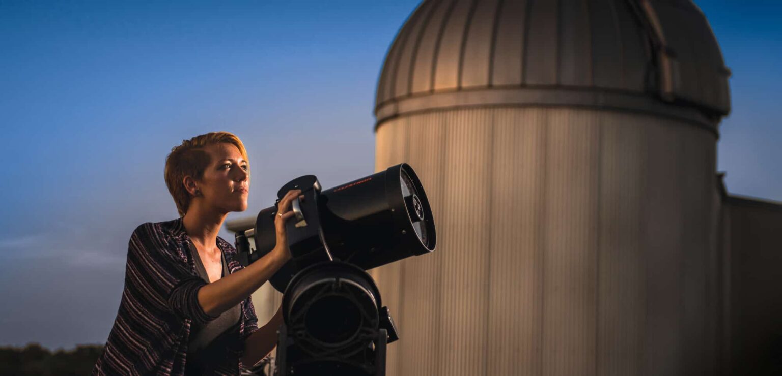 A female student looking up to the sky with a telescope.