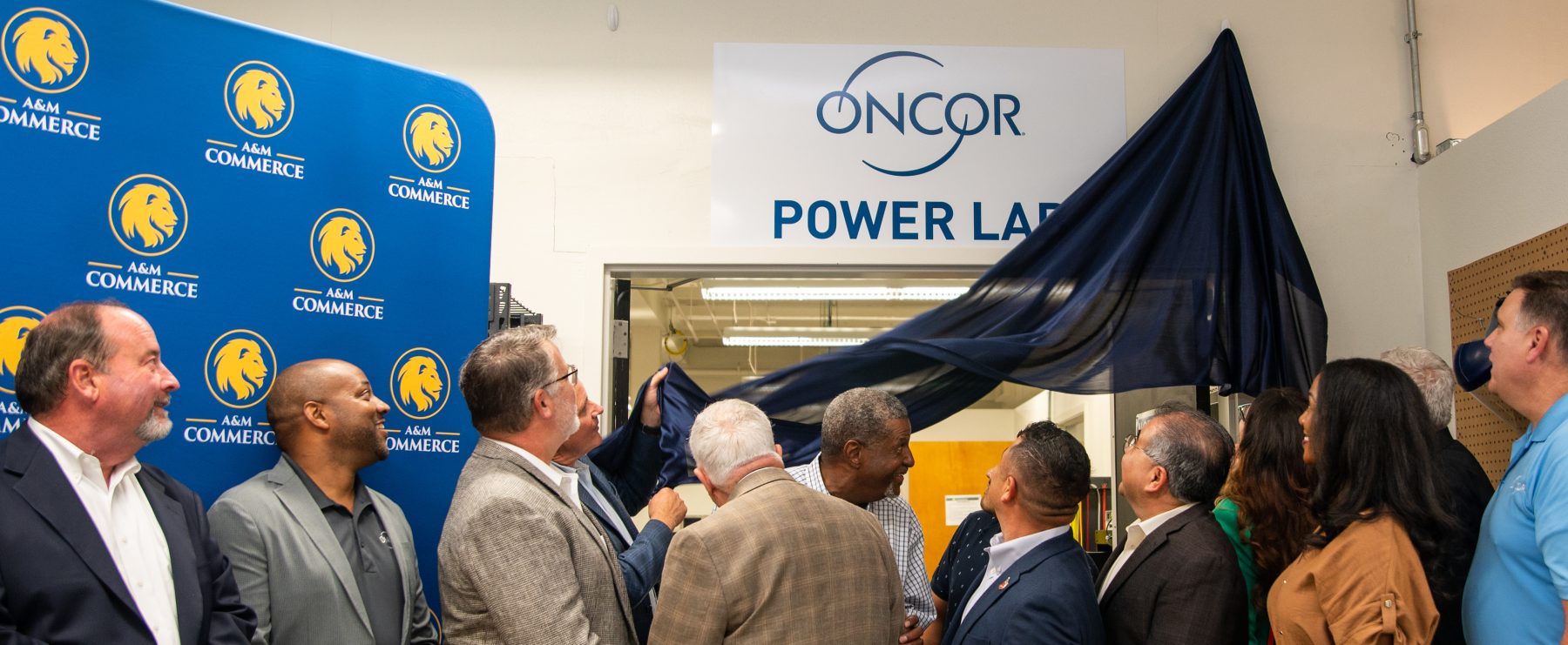 People look above doorway as curtain is pulled down to reveal "Oncor Power Lab" sign.