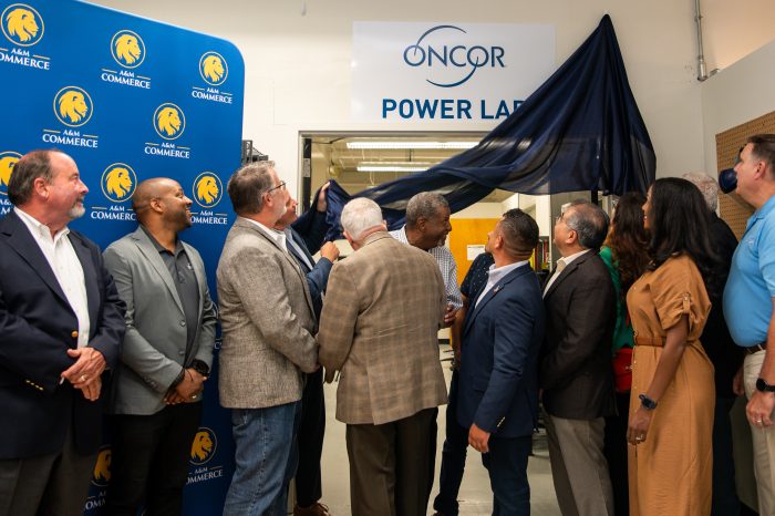 People look above doorway as curtain is pulled down to reveal "Oncor Power Lab" sign.