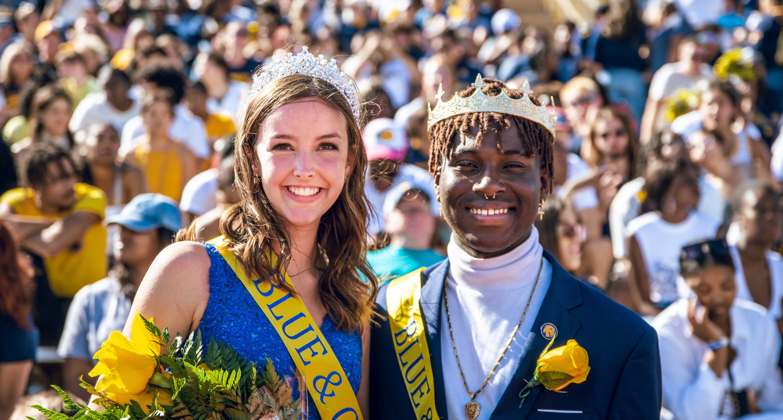 Two people in crowns and sashes pose for a photo