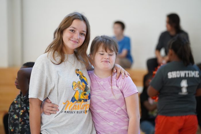 Two students share a hug side-by-side while posing for a photo.