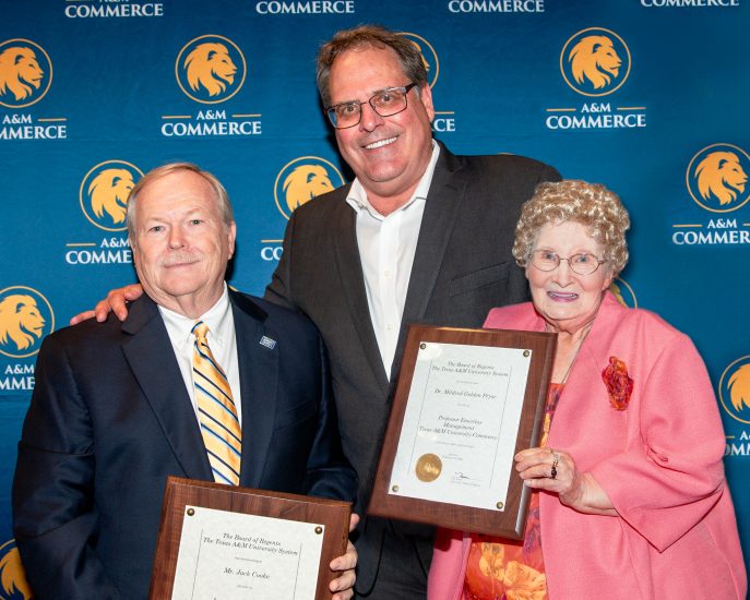 Three people pose for a photo. Two of the people are holding award plaques.