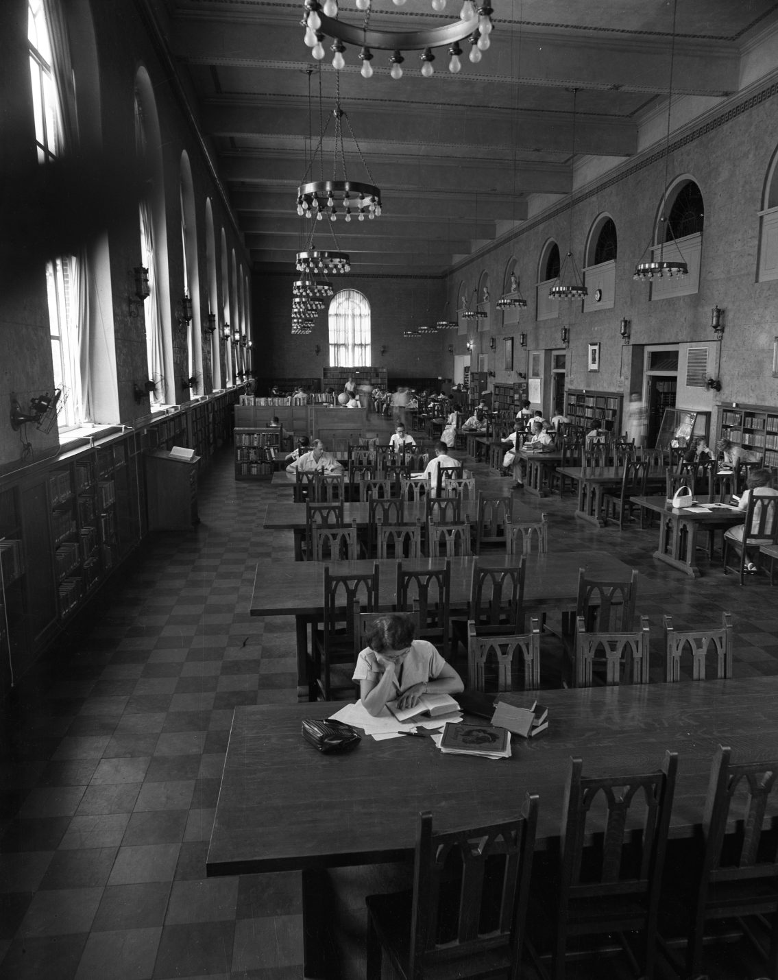 A black and white photo of a woman reading at a table