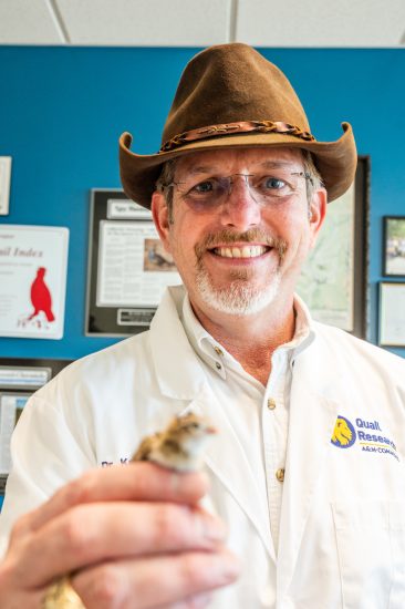 A man holds a newly hatched quail toward the viewer.