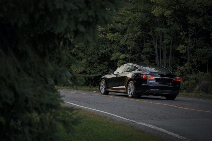 Side view of car driving down the road with a forest on either side.