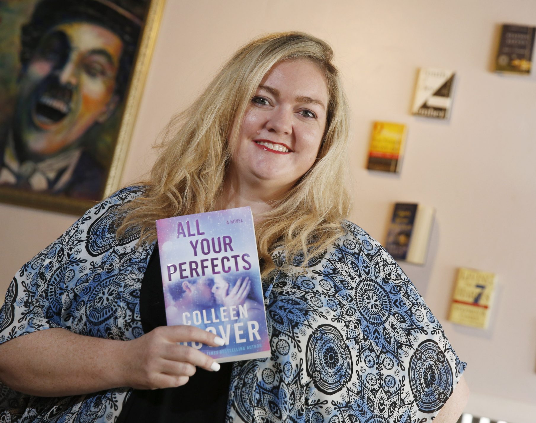 Colleen Hoover smiling and holding up her book "All Your Perfects"