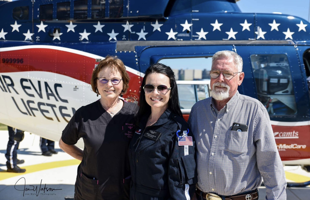A flight nurse stands between her proud parents in front of an emergency-evacuation helicopter.