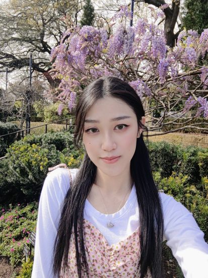 A woman taking a self-portrait with garden scenery behind her.