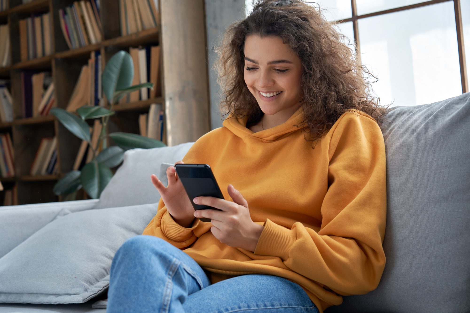 A female on the couch looking through her phone while smiling.