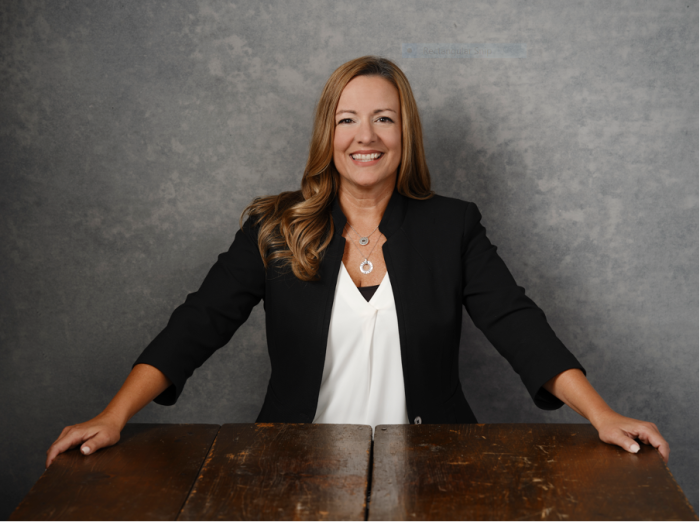 A woman stands behind a table with both hands on the edges.