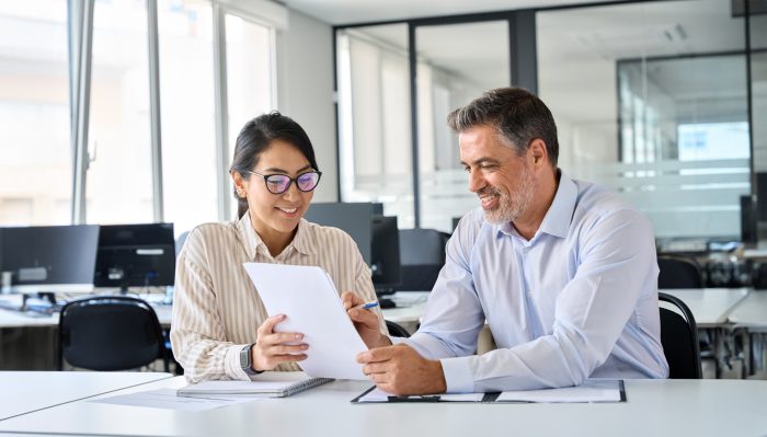 Two people at a desk look at a document together.