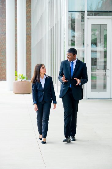 A female and male business dress walking outside talking.