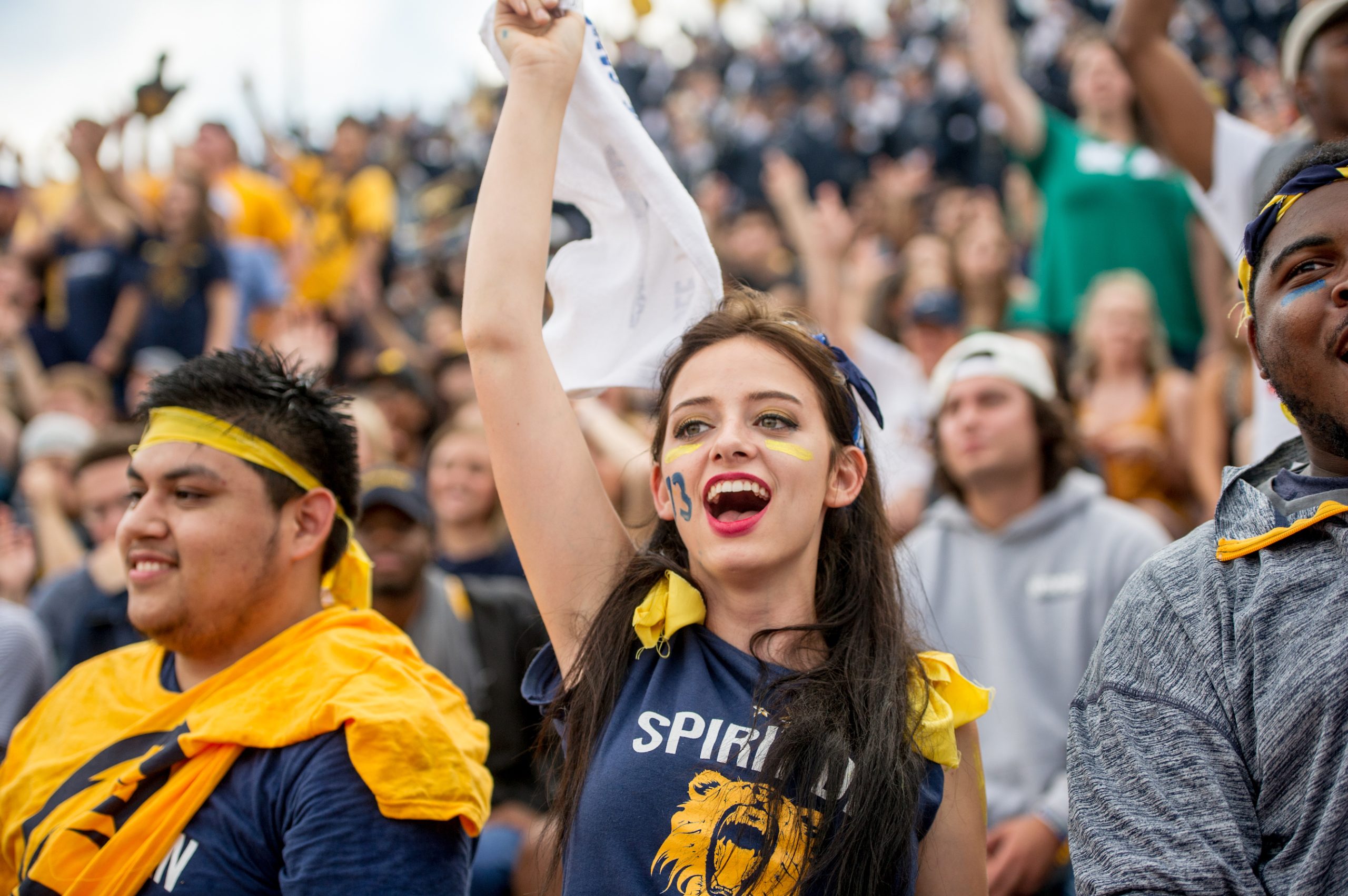 A Female student waving a flag and cheering at the foot ball stadium.