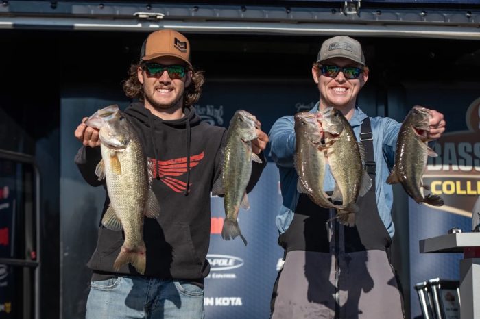 Two people hold a largemouth bass in each hand while posing for a photo.