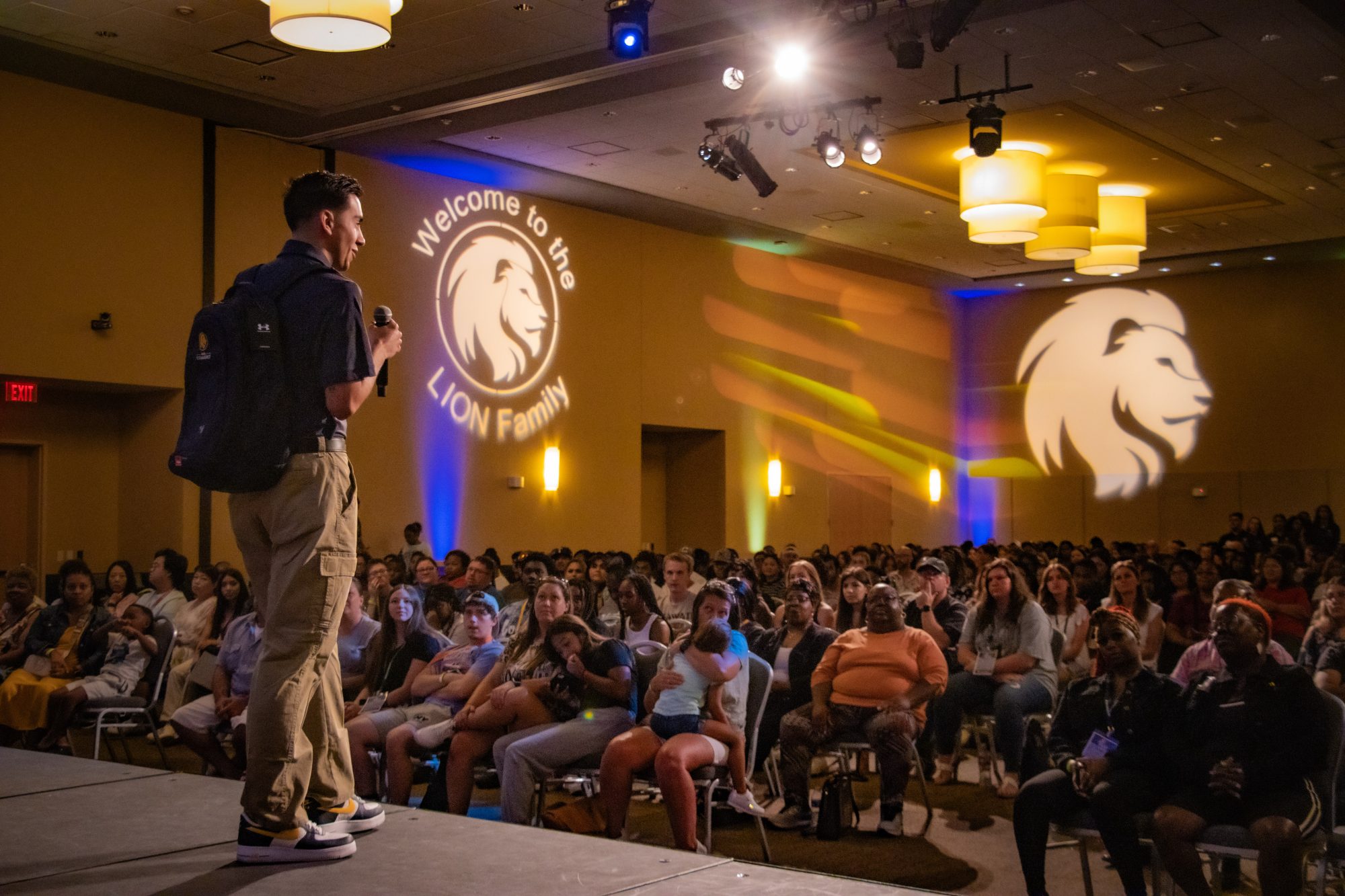 The class president leading the ROAR presentation from the stage with a large crowd in front of him. The TAMUC logo lit up in the background on the wall.