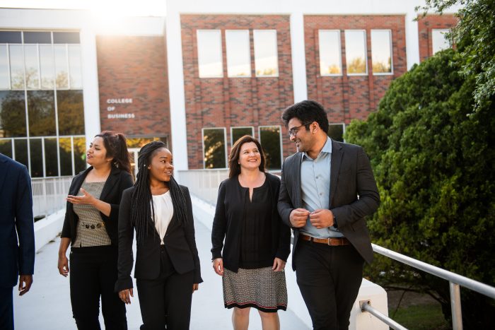 A big of students walking out of the business building smiling and talking.