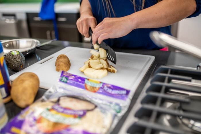 Hands pictured using a knife to cut potatoes.