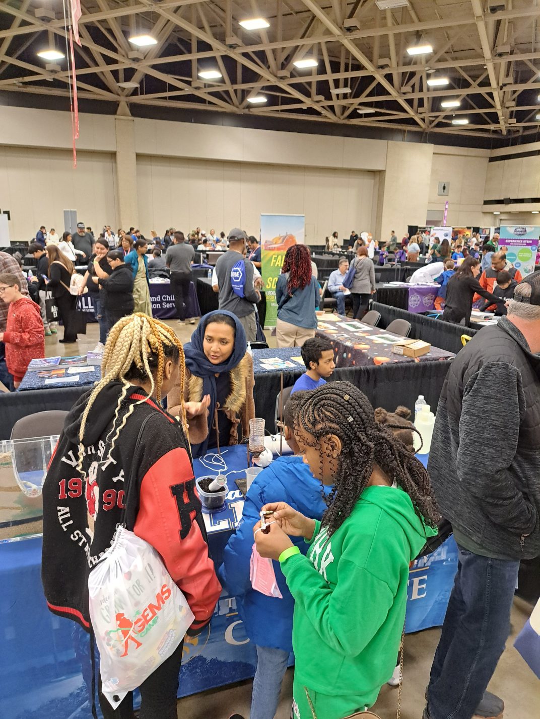 A faculty member talks to children congregating at a table displaying various science demonstrations.