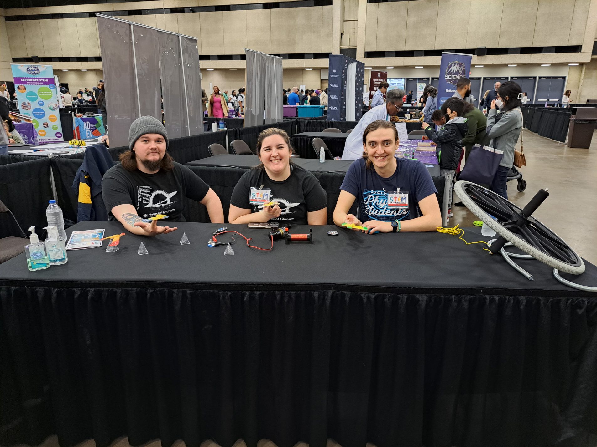 College students sit at a table displaying various science demonstrations.