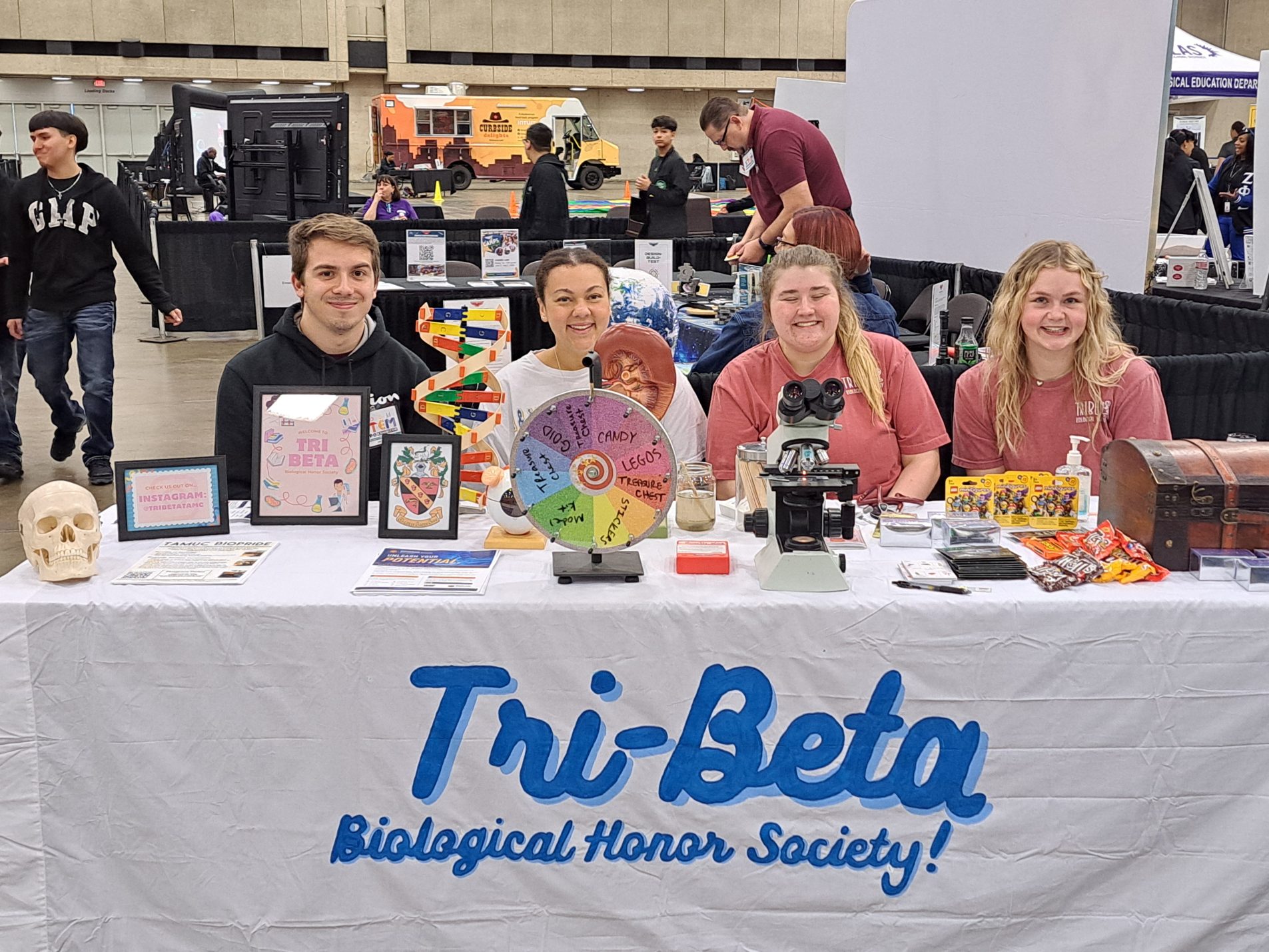 College students sit at a table displaying various science demonstrations.