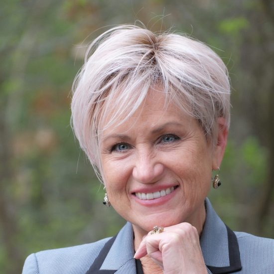 A woman poses against a backdrop of greenery.