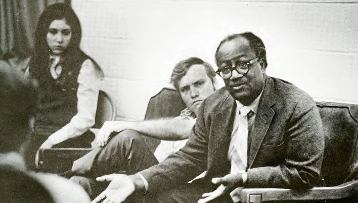 Black and white photo of David Talbot sitting with a group of students talking