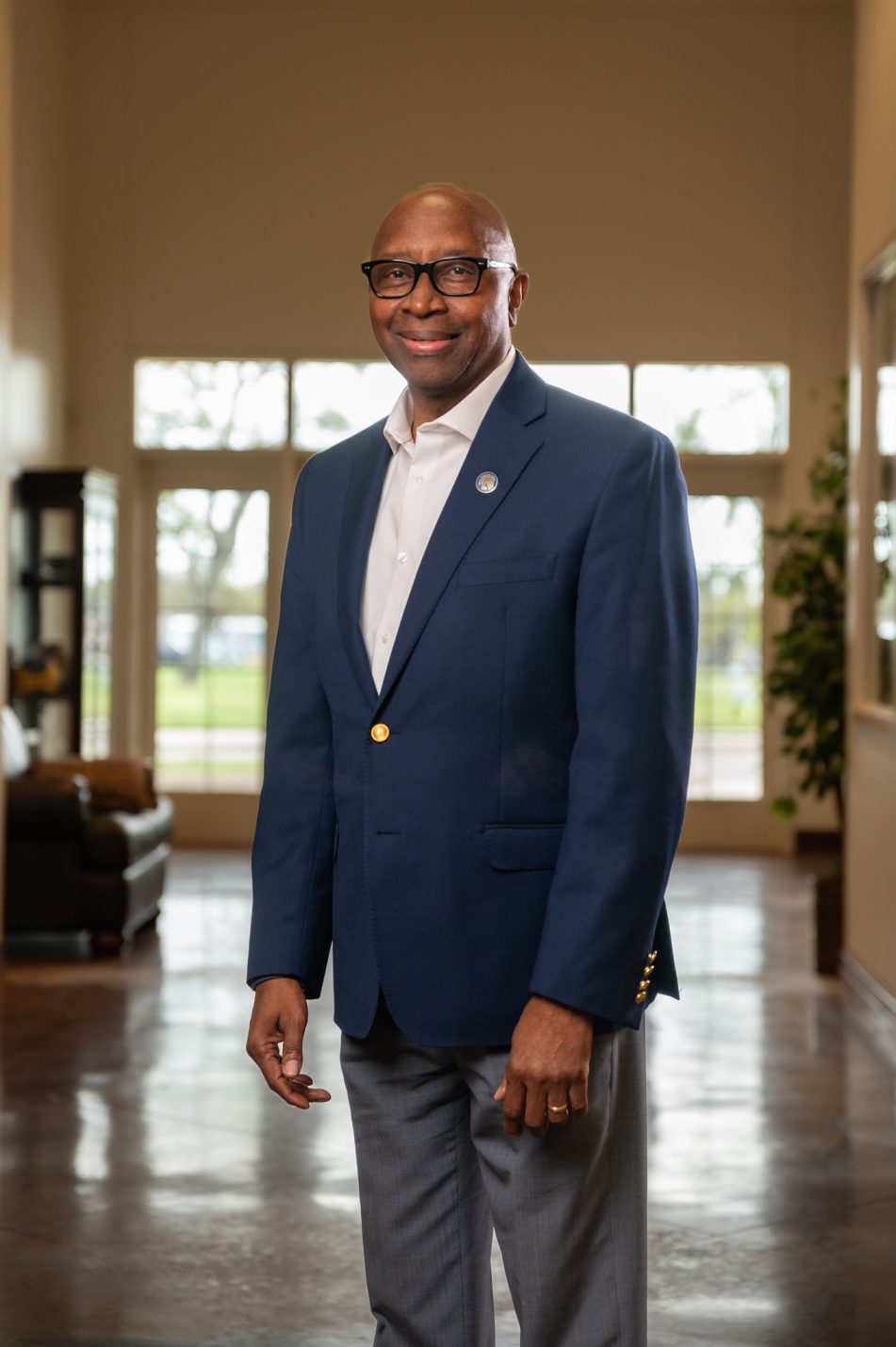 Derryle Peace faces the camera and smiles. He is wearing a suit jacket and his arms are hanging down at his sides.