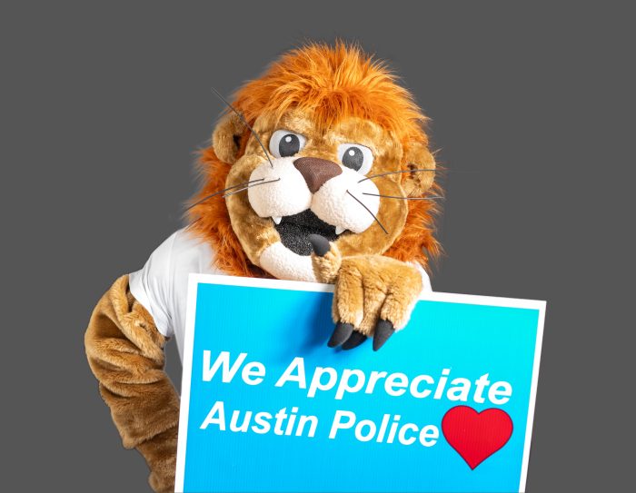 The Lucky Lion mascot holds a sign saying "We Appreciate Austin Police"