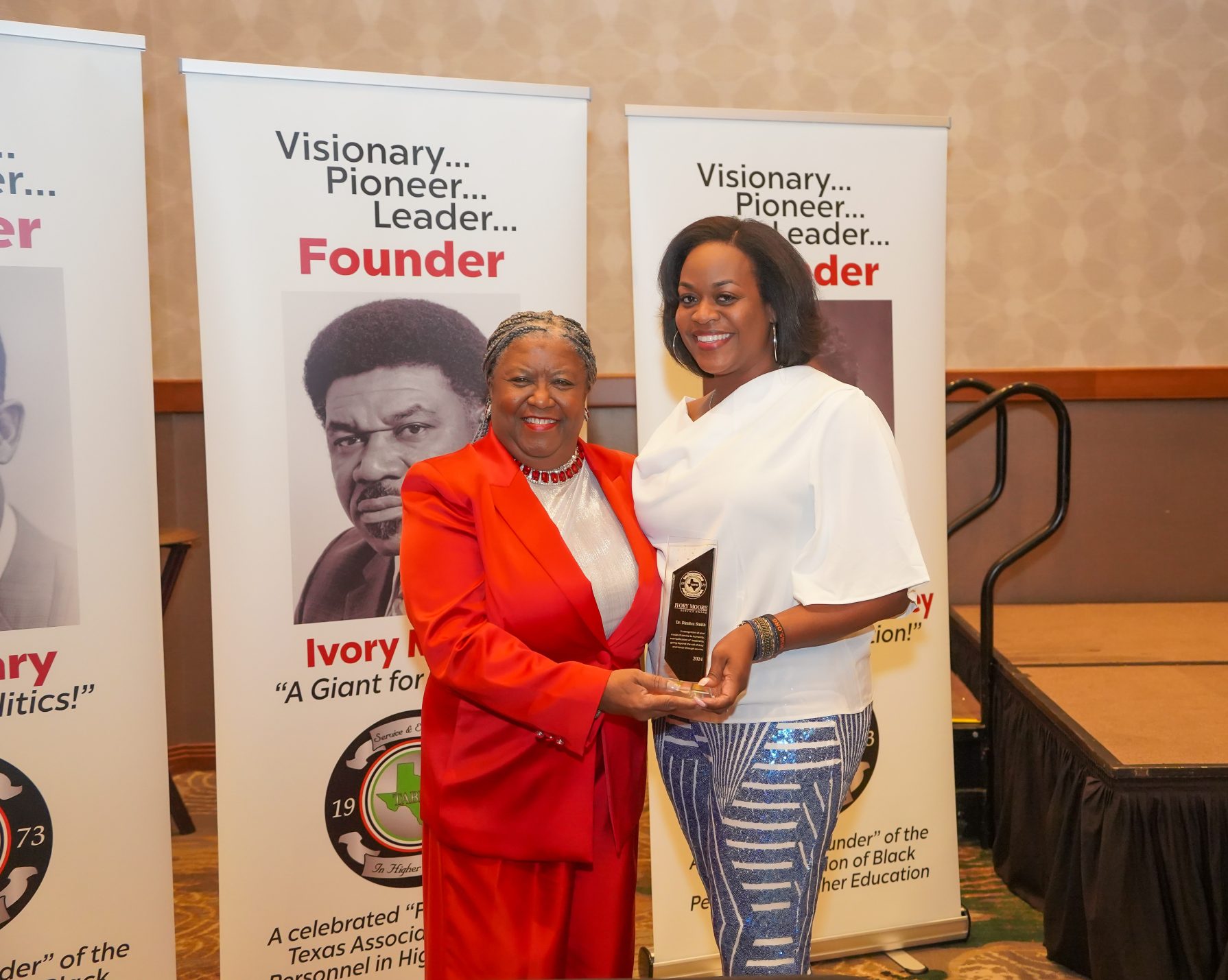 Two women stand holding an award between them.