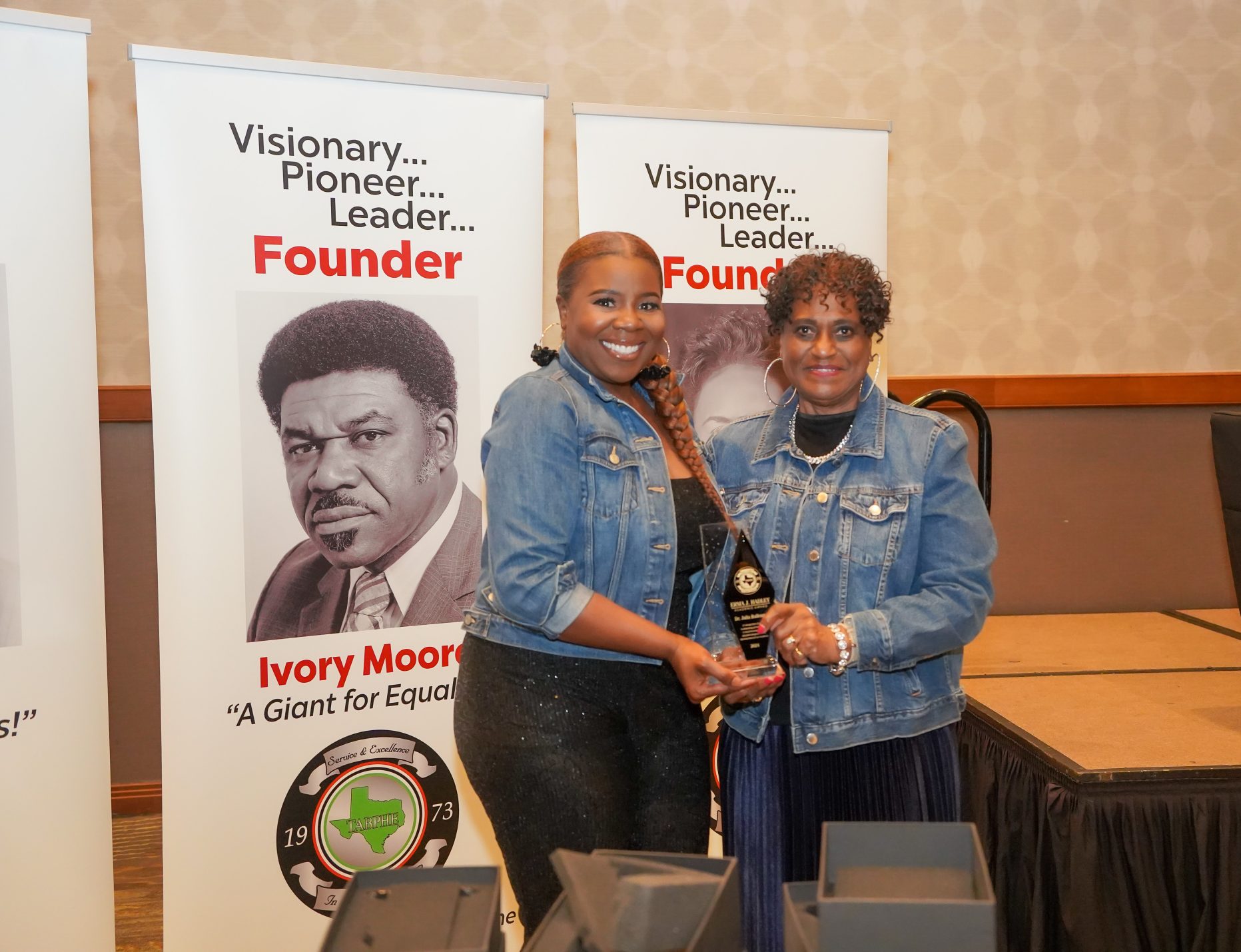 Two women stand holding an award between them.