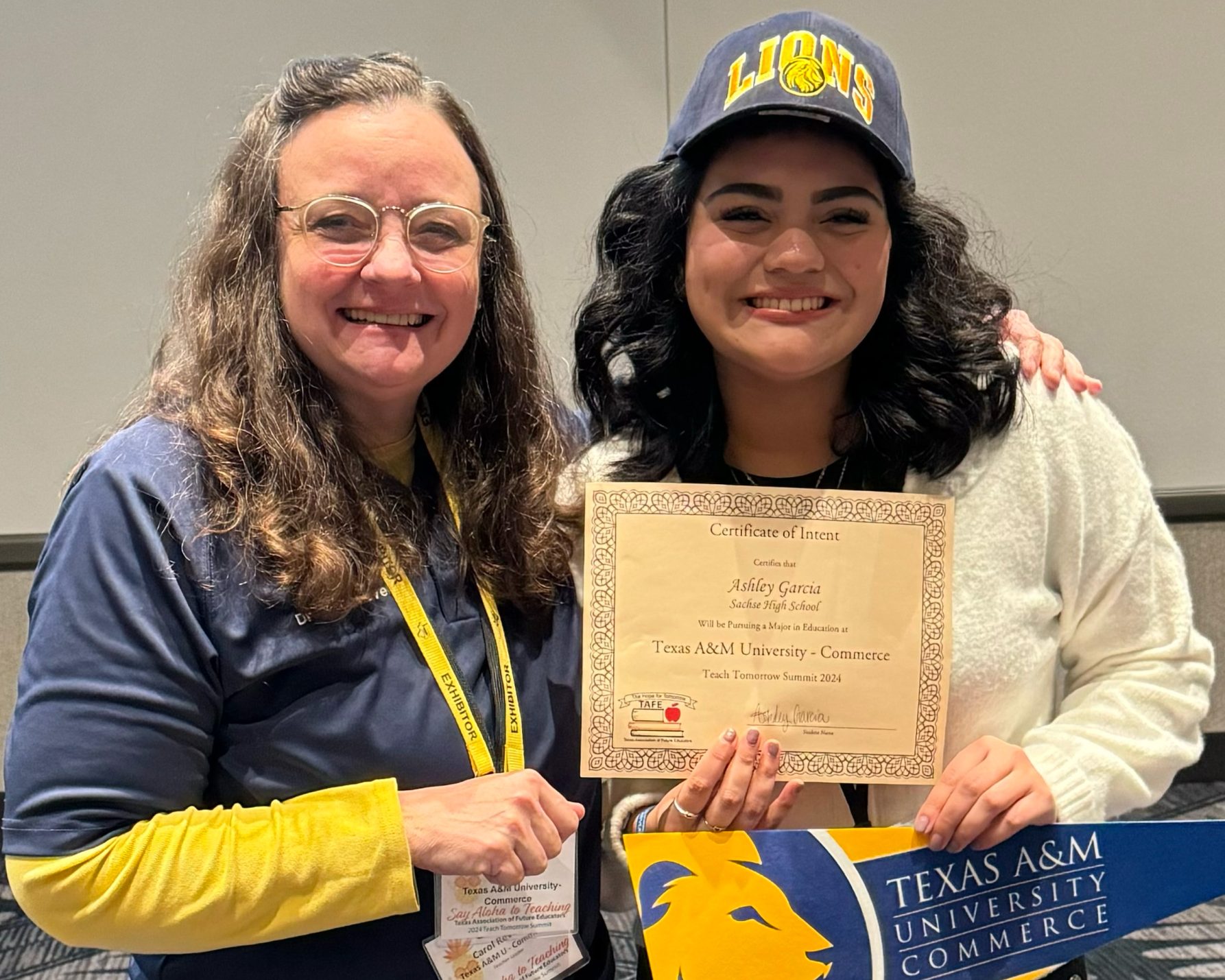 A professor and graduating high school senior stand side by side with certificate affirming the student's college commitment.