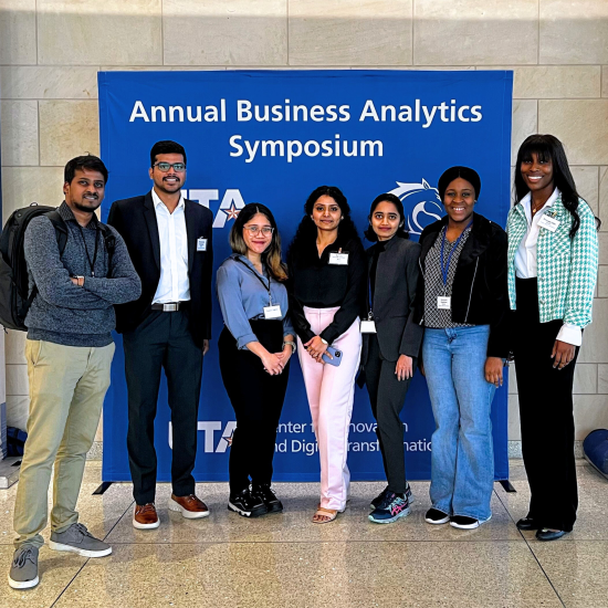 A group of people pose for a photo in front of a banner that reads "Annual Business Analytics Symposium."