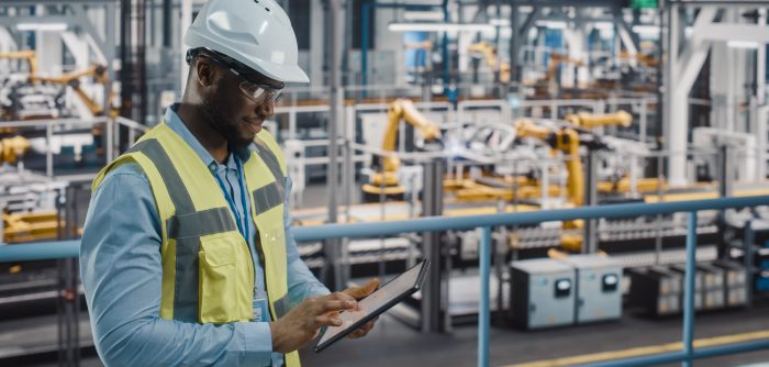 A male safety and health worker overseeing a factory assembly line.