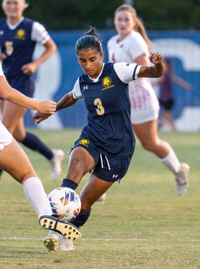 Soccer player kicks the ball as opponent tries to block.