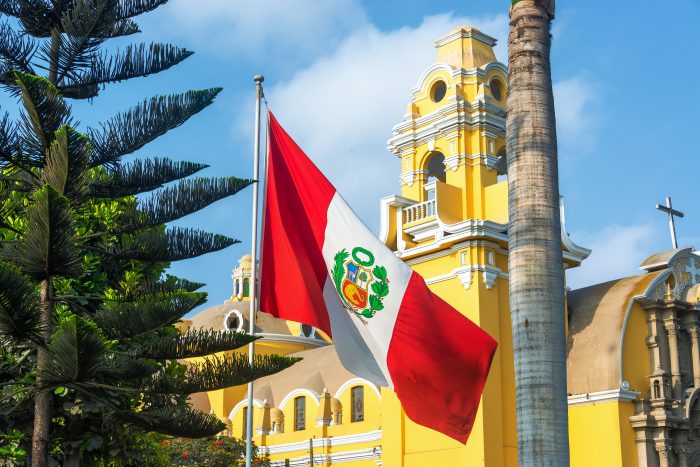 Peruvian flag flying in front of a yellow building