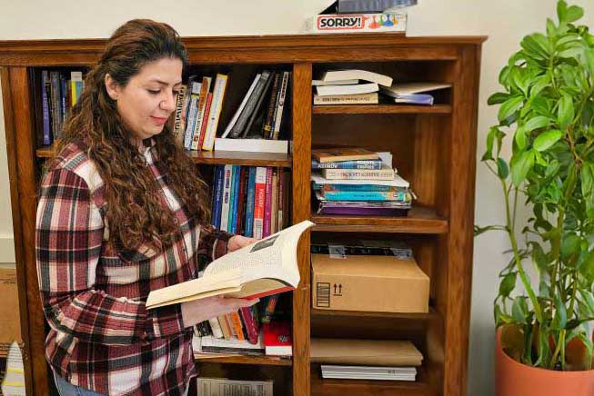 A female looking down at a book in front of a book shelf.