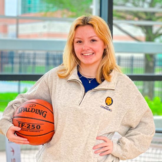 A young woman poses holding a basketball on her hip.