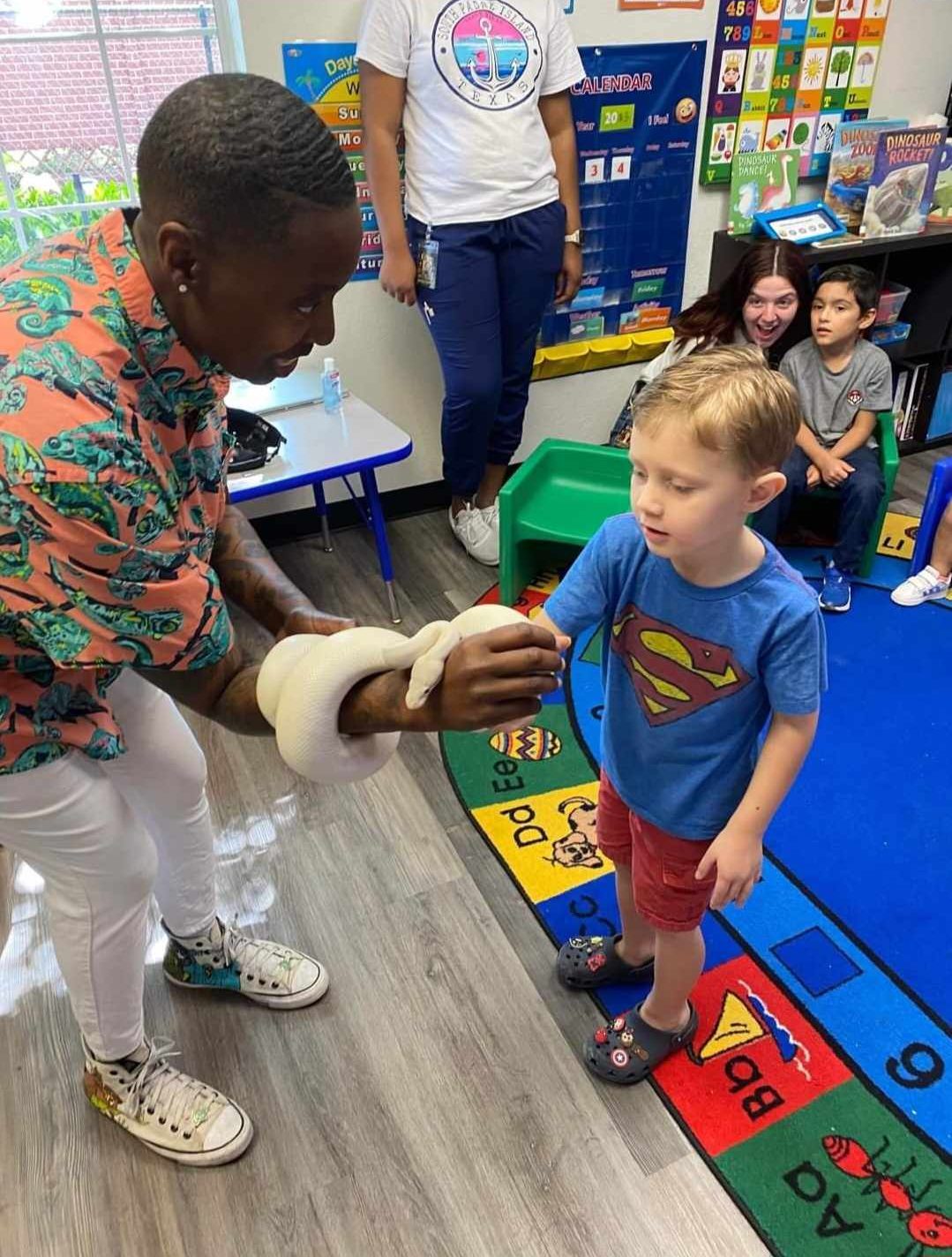 A woman safely introduces a white snake to an elementary classroom. A young boy stands ready to pet the snake.