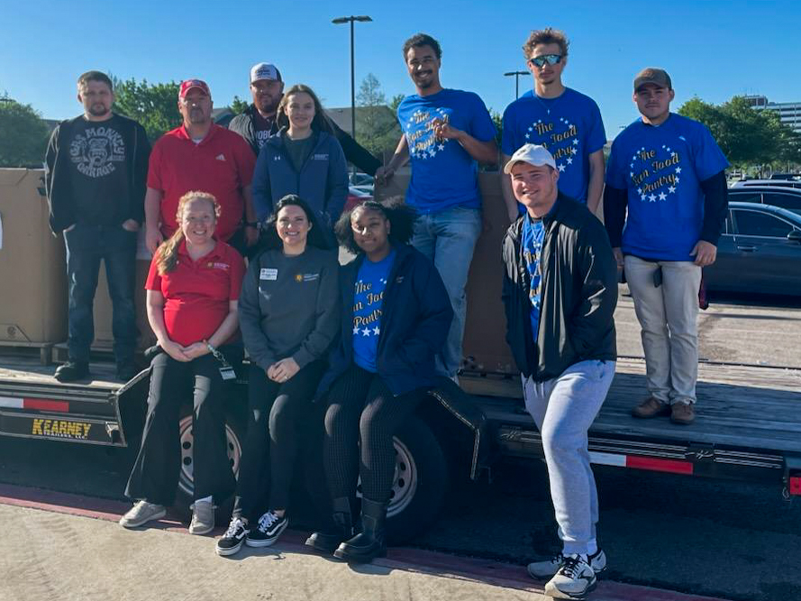 A group of volunteers stand on and around a trailer loaded with boxes from a food drive.