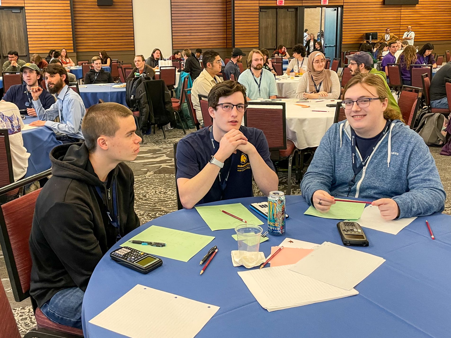 Three students sit at a table with calculators, paper and pencils.