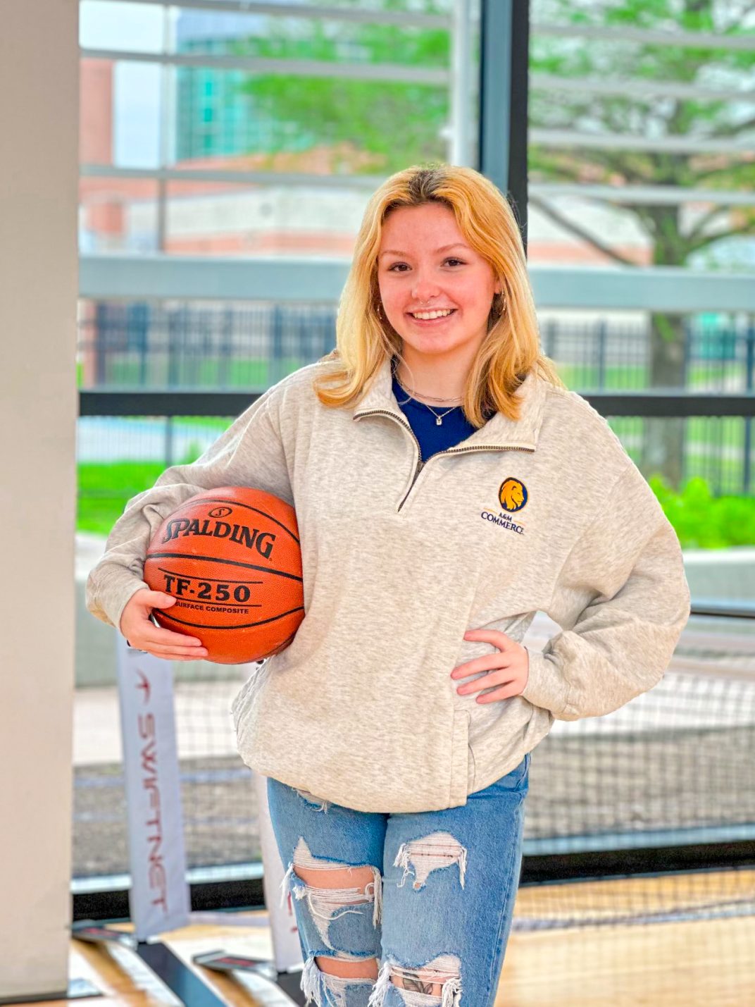 A young woman poses, holding a basketball on her hip.