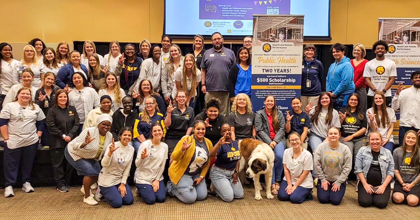 A large group of college students, faculty and staff posing while displaying the "Lucky Lion" hand symbol.