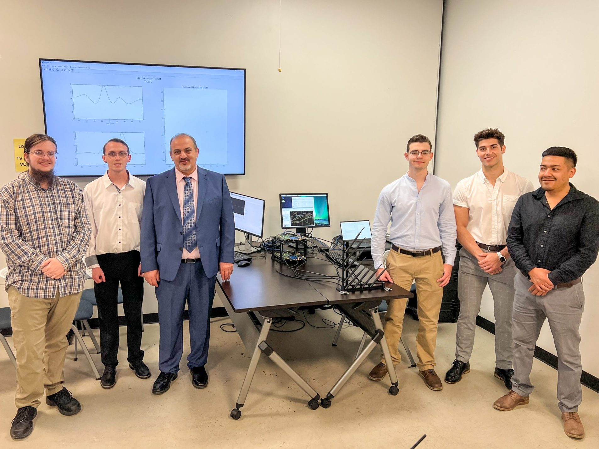 Four college students and their faculty advisor stand alongside their project spread across a tabletop.